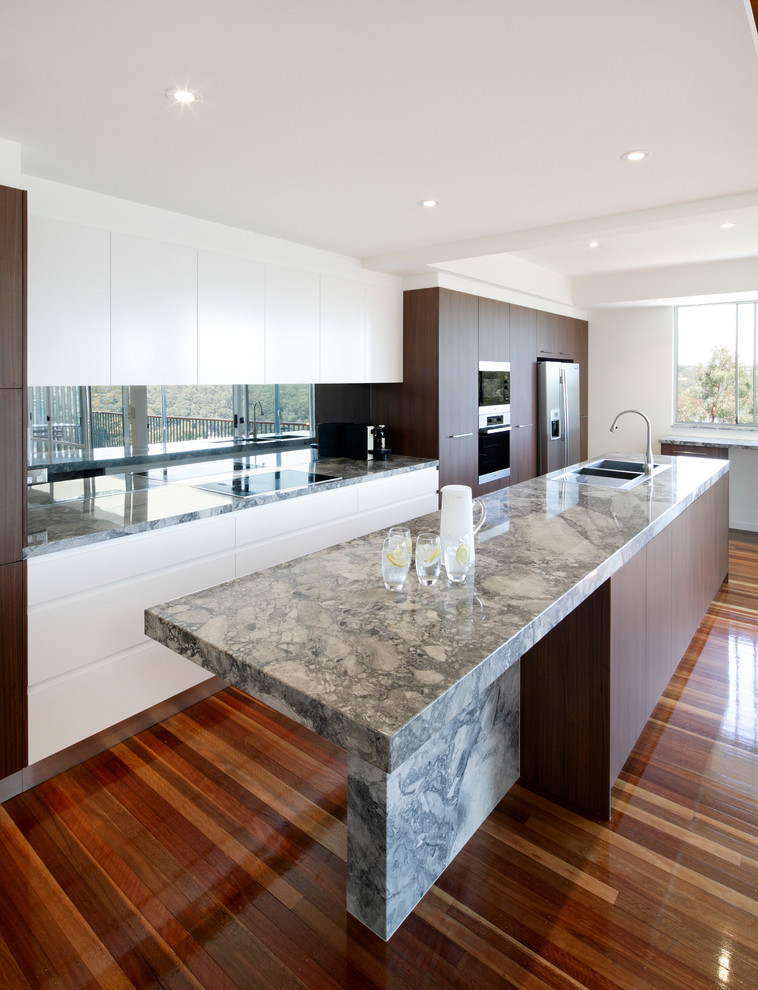 Idéer för funkis kök, med marmorbänkskiva, stänkskydd med metallisk yta, spegel som stänkskydd, mellanmörkt trägolv och en köksö