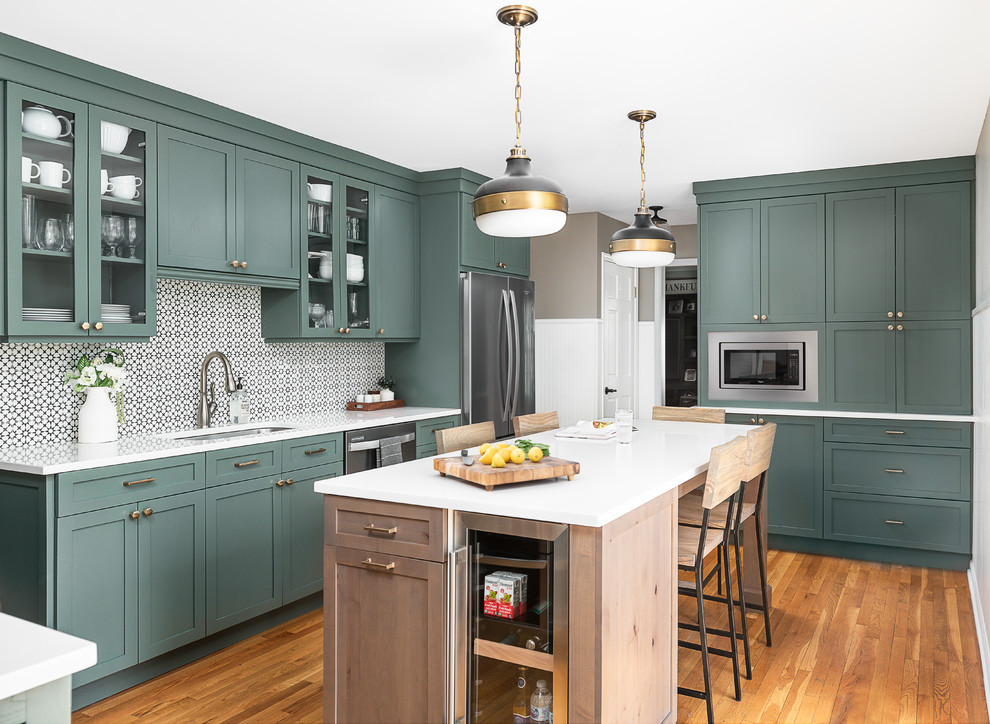 Photo of a medium sized traditional l-shaped enclosed kitchen in Chicago with a submerged sink, shaker cabinets, green cabinets, engineered stone countertops, white splashback, cement tile splashback, stainless steel appliances, light hardwood flooring, an island and white worktops.