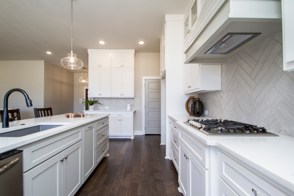 Photo of a large traditional u-shaped kitchen/diner in Little Rock with a submerged sink, recessed-panel cabinets, white cabinets, engineered stone countertops, grey splashback, ceramic splashback, stainless steel appliances, dark hardwood flooring, an island, brown floors and white worktops.
