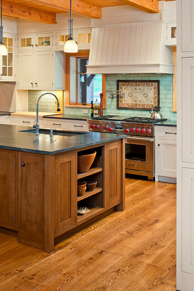 Exempel på ett klassiskt kök, med en undermonterad diskho, vita skåp, bänkskiva i täljsten, blått stänkskydd, stänkskydd i tunnelbanekakel, rostfria vitvaror, mellanmörkt trägolv och en köksö