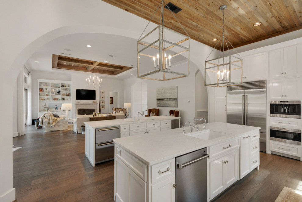 Inspiration for a large beach style u-shaped kitchen/diner in Other with a submerged sink, shaker cabinets, white cabinets, white splashback, stainless steel appliances, medium hardwood flooring and multiple islands.