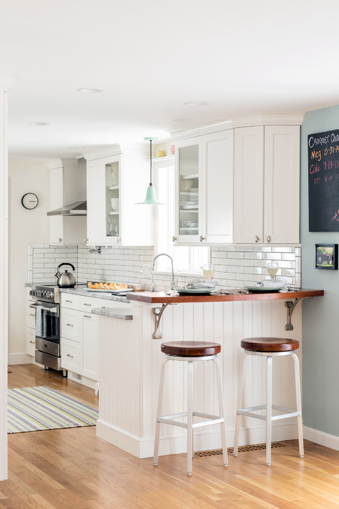 Diseño de cocina costera con armarios estilo shaker, puertas de armario blancas, salpicadero blanco, salpicadero de azulejos tipo metro y suelo de madera clara