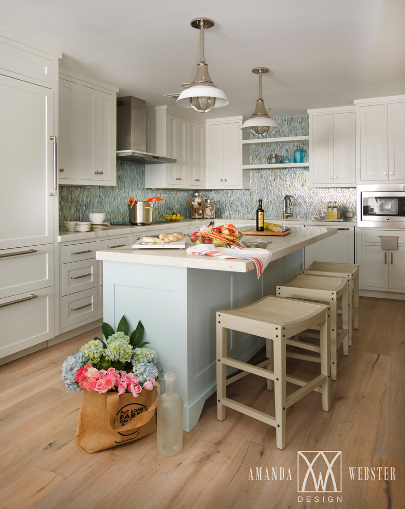 Foto på ett maritimt kök med öppen planlösning, med en undermonterad diskho, skåp i shakerstil, vita skåp, marmorbänkskiva, blått stänkskydd, stänkskydd i glaskakel, rostfria vitvaror, ljust trägolv och en köksö