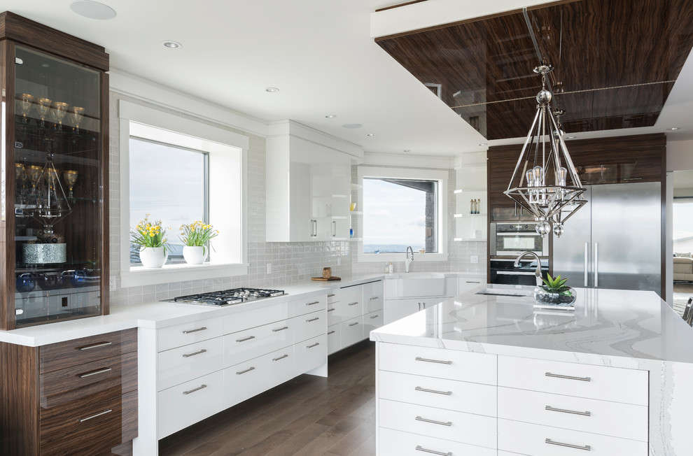 This is an example of an expansive modern u-shaped open plan kitchen in Other with a submerged sink, flat-panel cabinets, white cabinets, engineered stone countertops, white splashback, glass tiled splashback, stainless steel appliances, dark hardwood flooring, an island and white worktops.