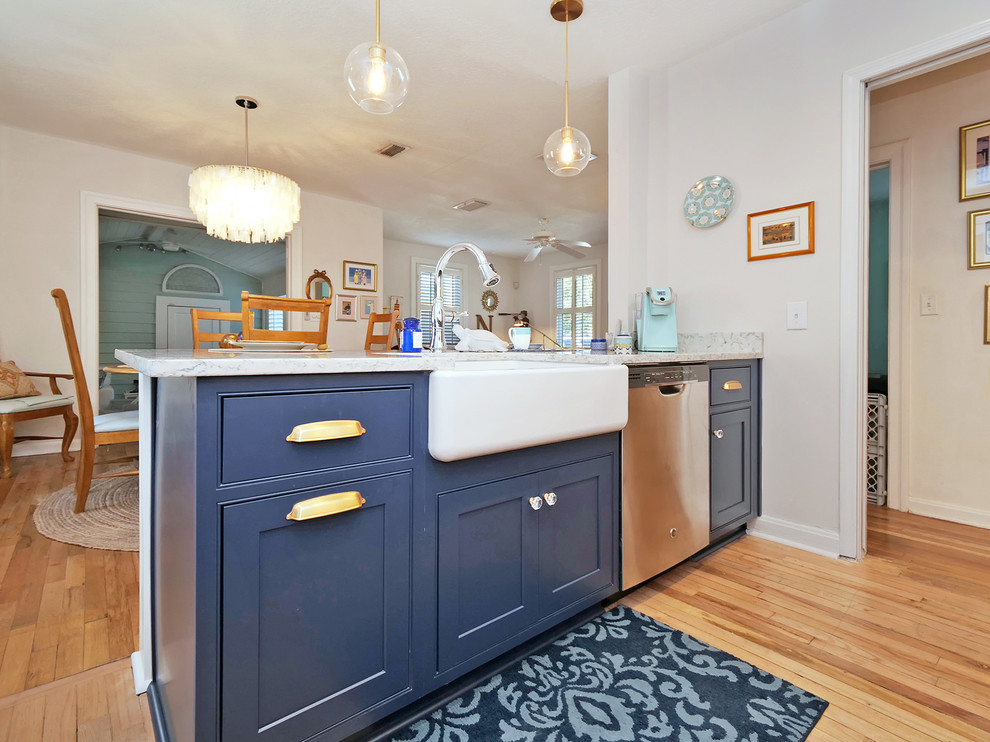 Foto på ett litet maritimt vit kök, med en rustik diskho, luckor med profilerade fronter, blå skåp, bänkskiva i kvarts, vitt stänkskydd, stänkskydd i tunnelbanekakel, rostfria vitvaror, mellanmörkt trägolv, en halv köksö och beiget golv
