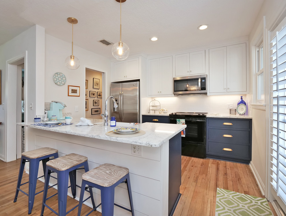 Photo of a small beach style galley kitchen/diner in Jacksonville with a belfast sink, beaded cabinets, blue cabinets, engineered stone countertops, white splashback, metro tiled splashback, stainless steel appliances, medium hardwood flooring, a breakfast bar, beige floors and white worktops.