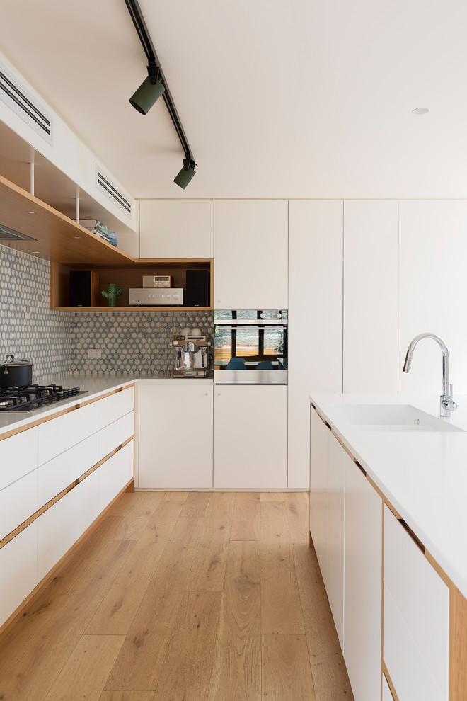 Example of a mid-sized trendy galley light wood floor and brown floor kitchen design in Sydney with an island and white countertops