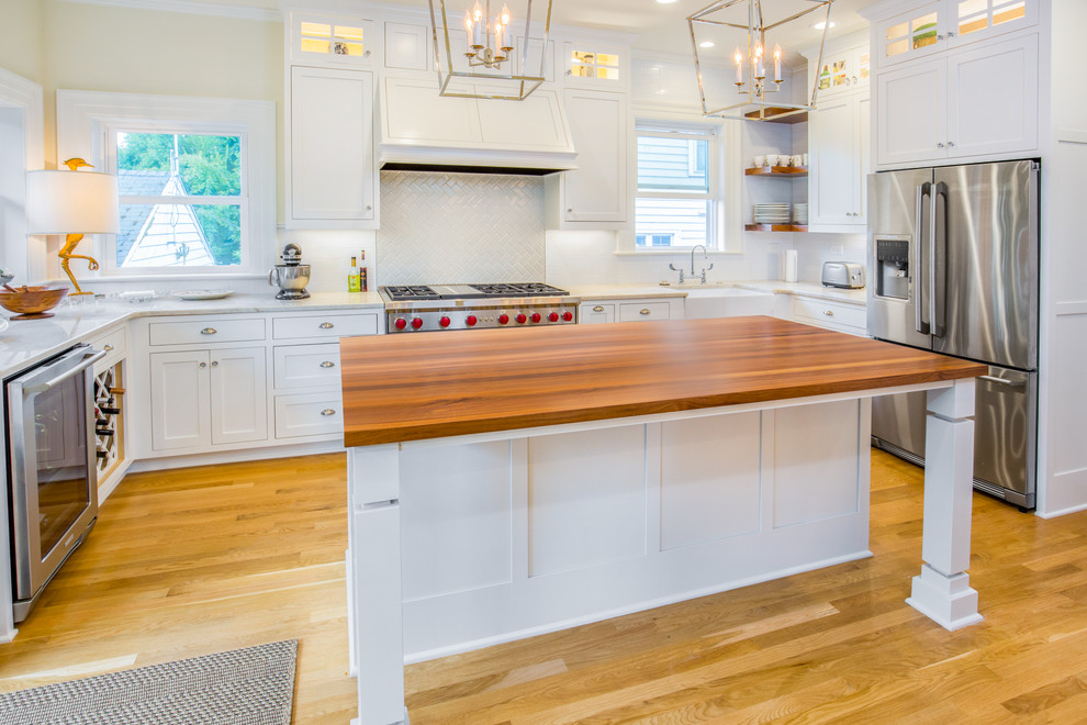 Mid-sized cottage u-shaped light wood floor and beige floor eat-in kitchen photo in Portland with a farmhouse sink, shaker cabinets, white cabinets, marble countertops, white backsplash, porcelain backsplash, stainless steel appliances and an island
