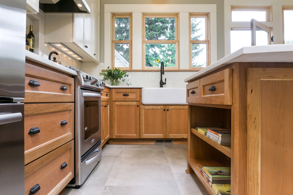 Bild på ett mellanstort amerikanskt l-kök, med en rustik diskho, skåp i mellenmörkt trä, bänkskiva i kvarts, vitt stänkskydd, stänkskydd i keramik, rostfria vitvaror, klinkergolv i keramik, en köksö, luckor med infälld panel och grått golv