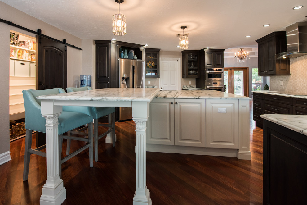 Inspiration for a large transitional u-shaped dark wood floor enclosed kitchen remodel in Tampa with a farmhouse sink, raised-panel cabinets, white cabinets, quartzite countertops, white backsplash, stone tile backsplash, stainless steel appliances and an island