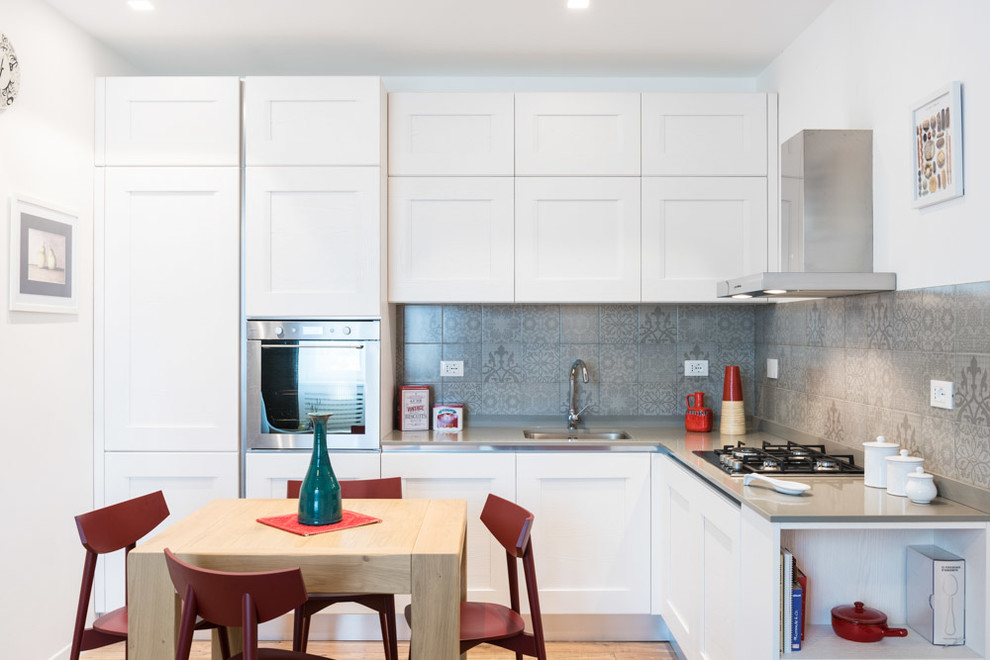 На фото: угловая кухня-гостиная в стиле неоклассика (современная классика) с одинарной мойкой, фартуком из керамической плитки и светлым паркетным полом без острова с