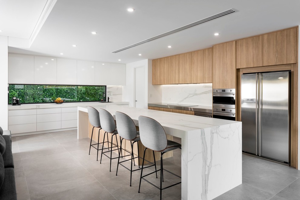 Foto di una grande cucina design con ante in legno chiaro, paraspruzzi bianco, paraspruzzi in lastra di pietra, elettrodomestici in acciaio inossidabile e pavimento grigio