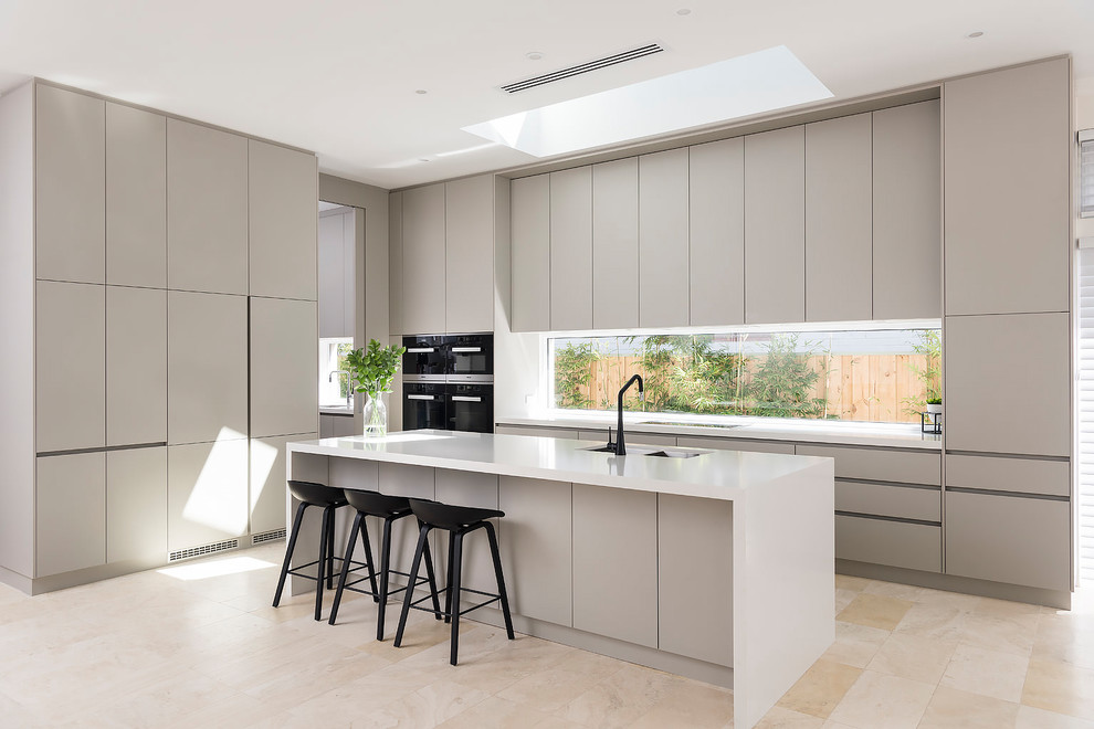 This is an example of a large contemporary galley open plan kitchen in Perth with a submerged sink, grey cabinets, engineered stone countertops, window splashback, travertine flooring, an island, beige floors, flat-panel cabinets and black appliances.