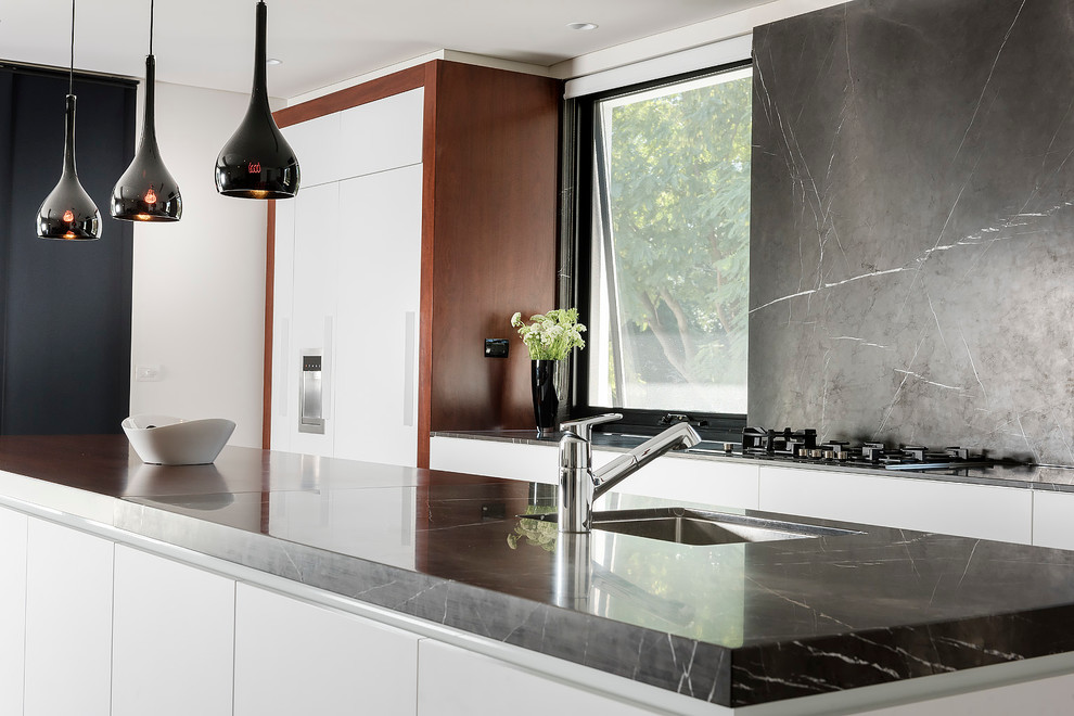 Modern inredning av ett stort grå grått kök, med en undermonterad diskho, släta luckor, vita skåp, marmorbänkskiva, grått stänkskydd, stänkskydd i marmor, svarta vitvaror, mellanmörkt trägolv, en köksö och grått golv