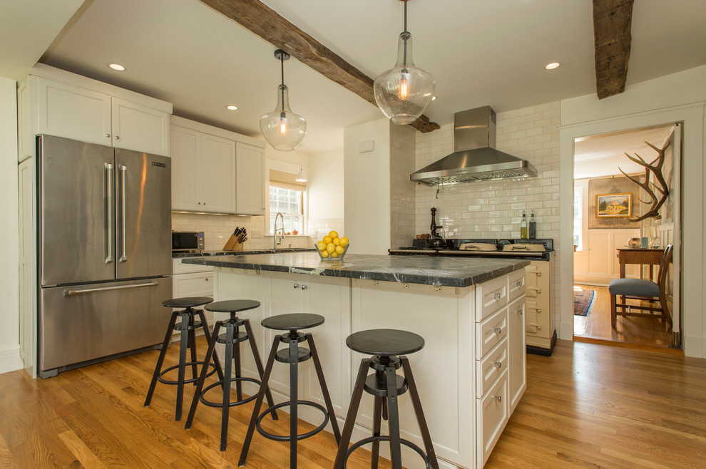 Eat-in kitchen - mid-sized transitional u-shaped medium tone wood floor eat-in kitchen idea in Boston with an undermount sink, shaker cabinets, white cabinets, soapstone countertops, white backsplash, ceramic backsplash, stainless steel appliances and an island