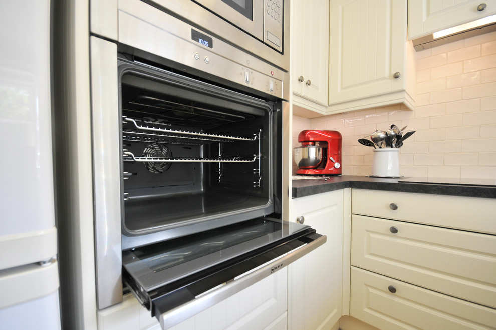 Foto på ett lantligt kök, med en nedsänkt diskho, beige stänkskydd, stänkskydd i tunnelbanekakel, rostfria vitvaror och klinkergolv i keramik