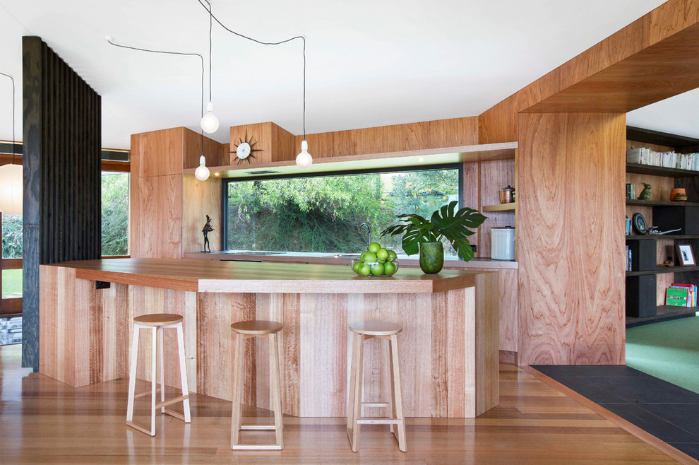На фото: параллельная кухня среднего размера с плоскими фасадами, светлыми деревянными фасадами, деревянной столешницей, паркетным полом среднего тона и островом