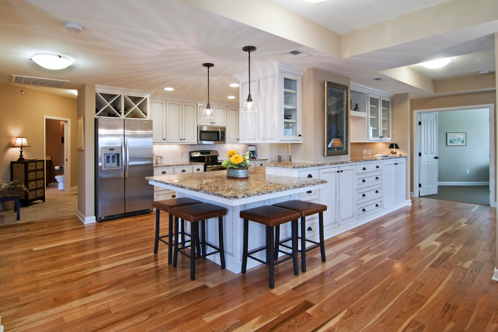 Exempel på ett stort klassiskt kök, med rostfria vitvaror, en undermonterad diskho, luckor med infälld panel, vita skåp, granitbänkskiva, vitt stänkskydd, stänkskydd i tunnelbanekakel, mellanmörkt trägolv och en halv köksö
