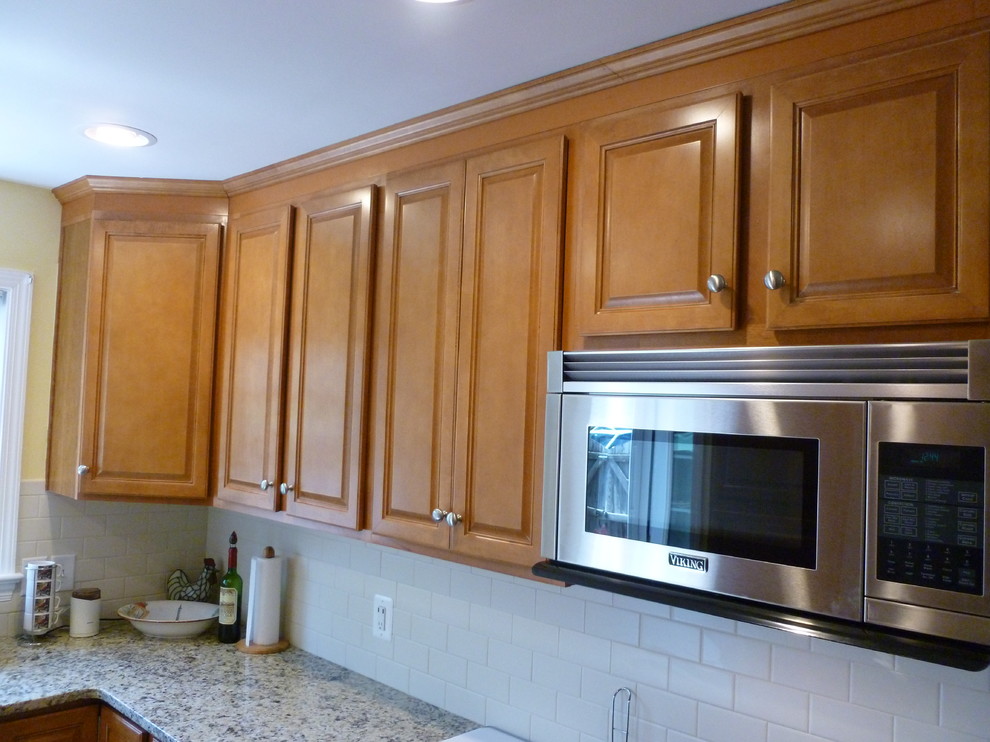 Inredning av ett klassiskt litet kök, med en nedsänkt diskho, luckor med upphöjd panel, skåp i mellenmörkt trä, granitbänkskiva, vitt stänkskydd, stänkskydd i keramik, rostfria vitvaror och mellanmörkt trägolv