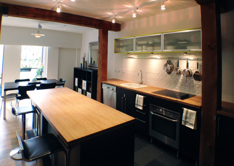 Medium sized modern galley kitchen/diner in Vancouver with a built-in sink, flat-panel cabinets, black cabinets, wood worktops, white splashback, porcelain splashback, stainless steel appliances, slate flooring and an island.