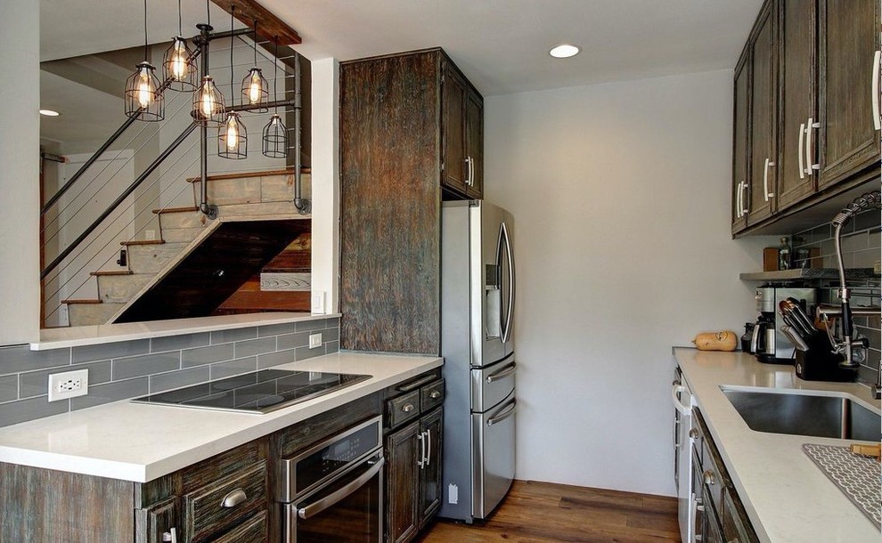 Inspiration for a medium sized rustic galley open plan kitchen in Santa Barbara with a submerged sink, raised-panel cabinets, distressed cabinets, engineered stone countertops, grey splashback, glass tiled splashback, stainless steel appliances, medium hardwood flooring and no island.