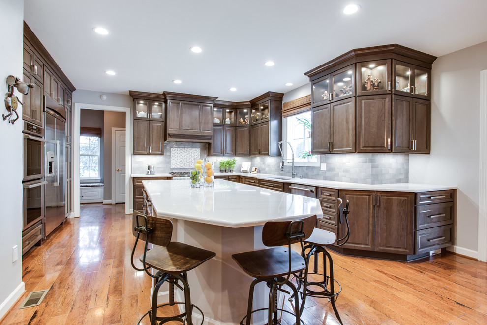Large u-shaped medium tone wood floor kitchen photo in DC Metro with an undermount sink, raised-panel cabinets, gray cabinets, quartz countertops, stainless steel appliances and an island