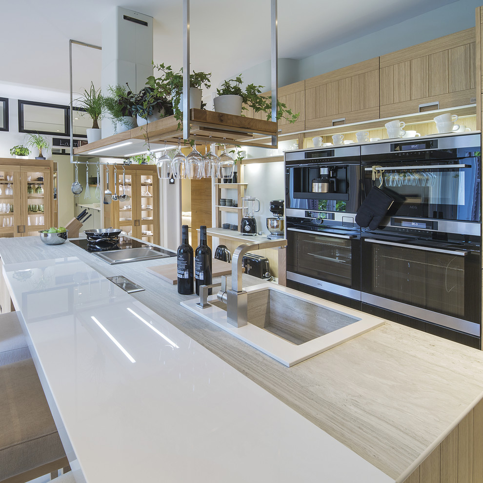 Пример оригинального дизайна: параллельная кухня-гостиная в современном стиле с накладной мойкой, плоскими фасадами, светлыми деревянными фасадами, черной техникой и островом