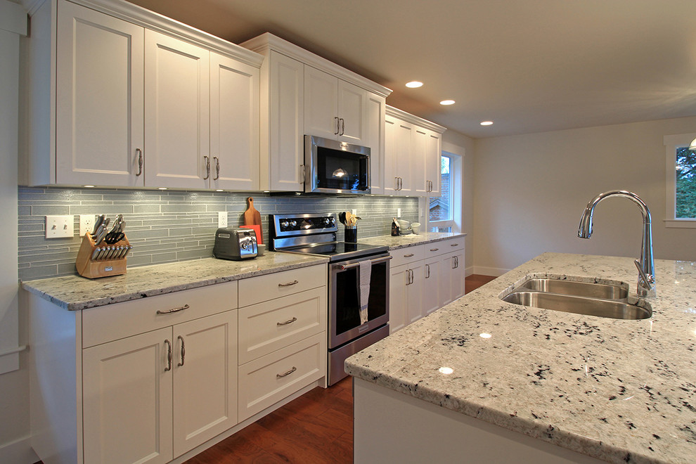 This is an example of a large nautical u-shaped open plan kitchen in Seattle with a submerged sink, shaker cabinets, white cabinets, granite worktops, grey splashback, mosaic tiled splashback, stainless steel appliances, medium hardwood flooring and an island.