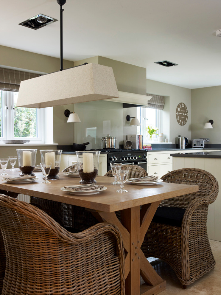 Design ideas for a large classic u-shaped open plan kitchen in Devon with a belfast sink, beaded cabinets, light wood cabinets, composite countertops, green splashback, glass sheet splashback, black appliances, limestone flooring and an island.