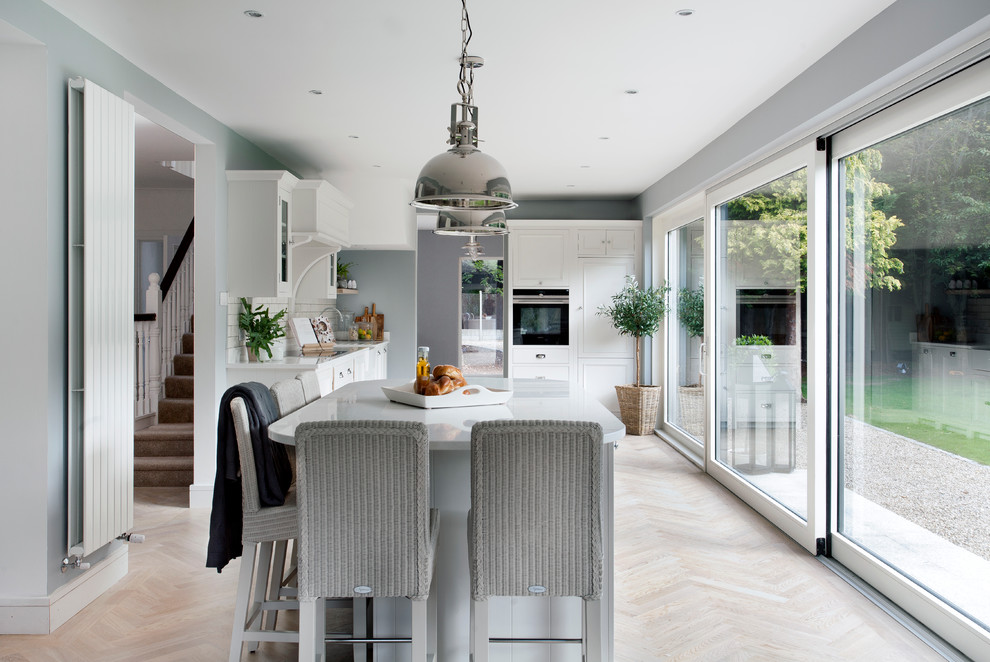 Inspiration for a mid-sized transitional l-shaped light wood floor and beige floor eat-in kitchen remodel in Dublin with recessed-panel cabinets, white cabinets, quartzite countertops, white backsplash, an island and subway tile backsplash