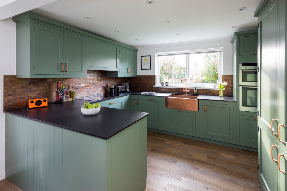 Inspiration for a medium sized traditional u-shaped kitchen/diner in Kent with a belfast sink, shaker cabinets, green cabinets, engineered stone countertops, metal splashback, lino flooring, a breakfast bar and green floors.