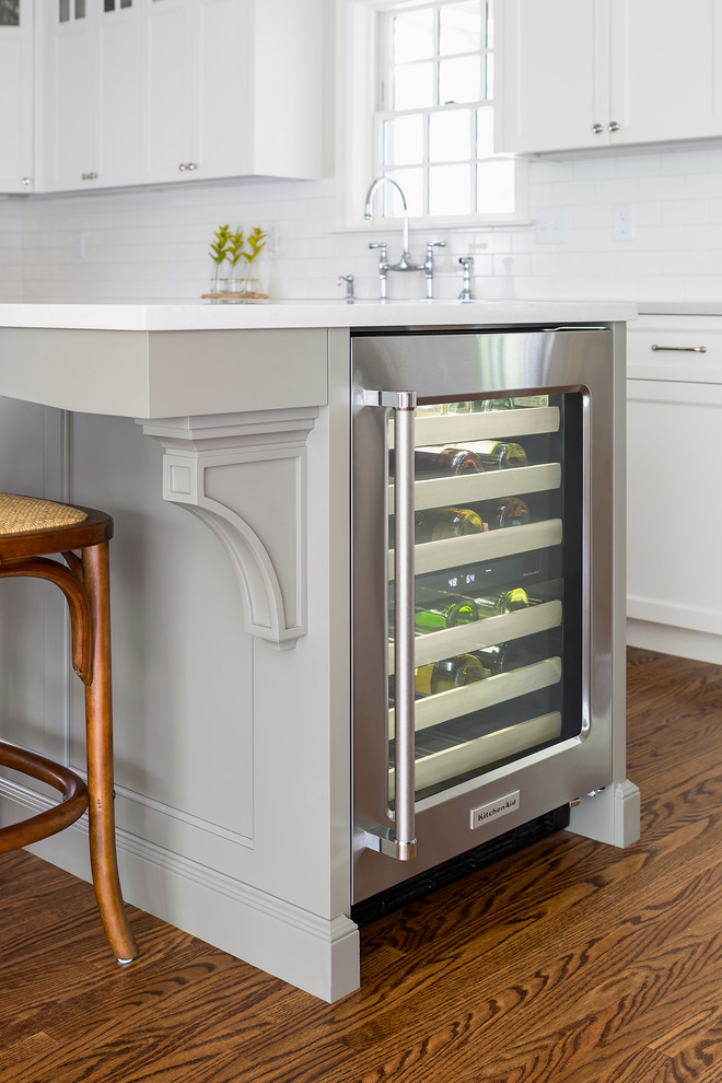 Mid-sized transitional l-shaped medium tone wood floor eat-in kitchen photo in Minneapolis with a farmhouse sink, white cabinets, white backsplash, subway tile backsplash, stainless steel appliances, an island, shaker cabinets and quartzite countertops
