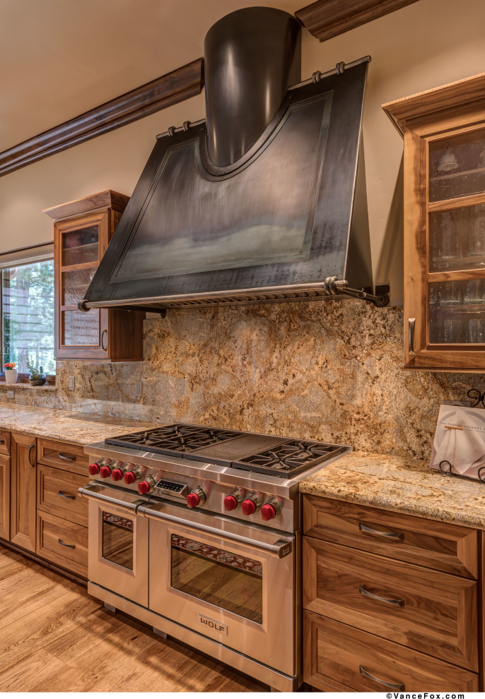 Example of a huge mountain style l-shaped medium tone wood floor and brown floor eat-in kitchen design in Other with an undermount sink, glass-front cabinets, medium tone wood cabinets, granite countertops, beige backsplash, stone slab backsplash, stainless steel appliances, two islands and beige countertops