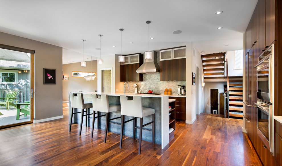 Mittelgroße Moderne Küchenbar mit flächenbündigen Schrankfronten, dunklen Holzschränken, Küchengeräten aus Edelstahl, braunem Holzboden, Kücheninsel, bunter Rückwand und orangem Boden in Denver