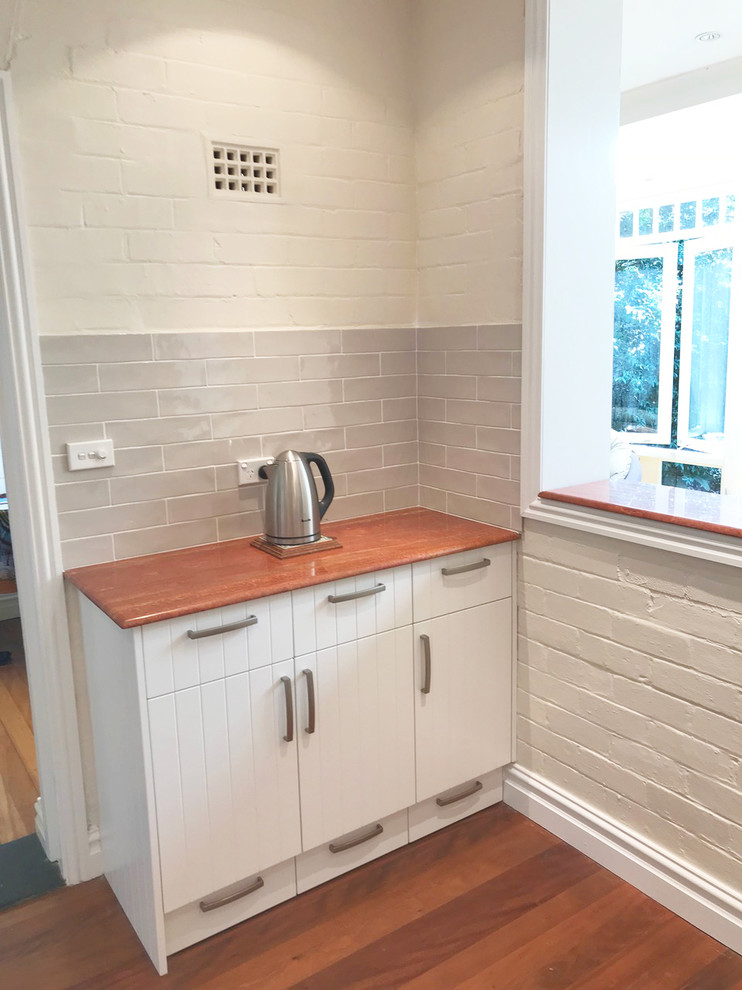 Cette photo montre une arrière-cuisine tendance avec des portes de placard blanches, une crédence beige, une crédence en céramique et un électroménager en acier inoxydable.