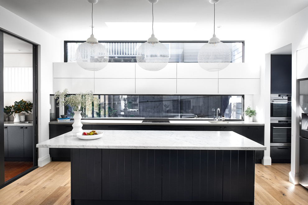 Bild på ett stort funkis grå grått l-kök, med en undermonterad diskho, marmorbänkskiva, fönster som stänkskydd, ljust trägolv, en köksö, släta luckor, svarta skåp, rostfria vitvaror och beiget golv