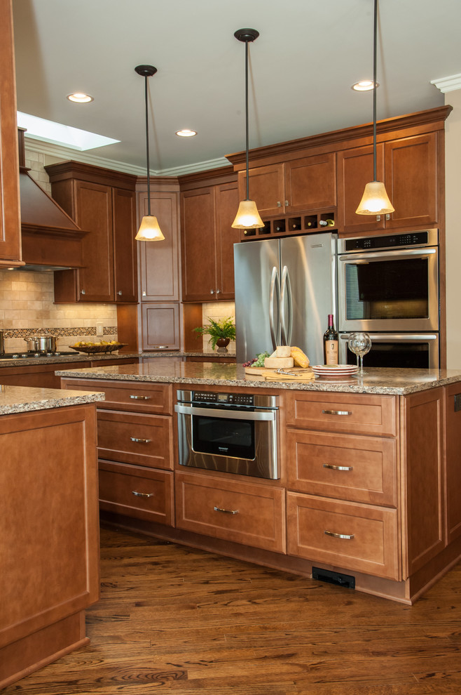 This is an example of a large classic u-shaped kitchen/diner in Detroit with a submerged sink, recessed-panel cabinets, medium wood cabinets, engineered stone countertops, brown splashback, metro tiled splashback, stainless steel appliances, medium hardwood flooring and an island.