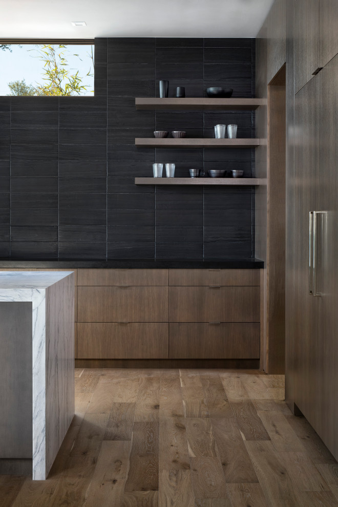 Exempel på ett stort modernt svart svart kök, med en undermonterad diskho, släta luckor, skåp i mellenmörkt trä, bänkskiva i täljsten, svart stänkskydd, stänkskydd i porslinskakel, integrerade vitvaror, mellanmörkt trägolv, en köksö och brunt golv