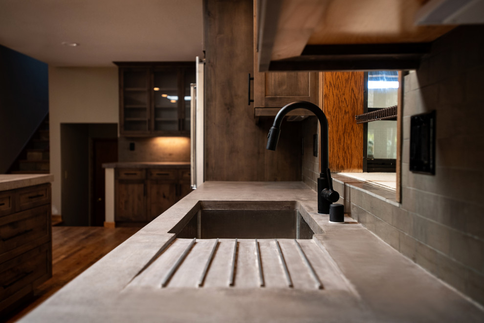 Photo of a large rustic galley open plan kitchen in Sacramento with a submerged sink, shaker cabinets, medium wood cabinets, concrete worktops, grey splashback, stone tiled splashback, stainless steel appliances, medium hardwood flooring, an island, multi-coloured floors and grey worktops.