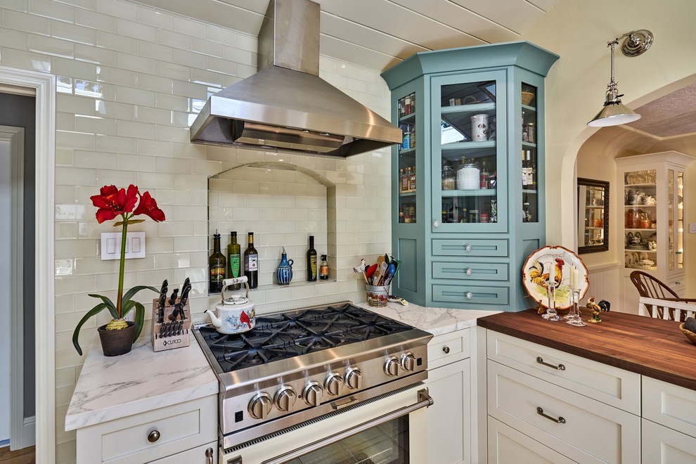 Example of a mid-sized cottage l-shaped ceramic tile eat-in kitchen design in San Francisco with a farmhouse sink, shaker cabinets, white cabinets, marble countertops, white backsplash, glass tile backsplash, stainless steel appliances and a peninsula