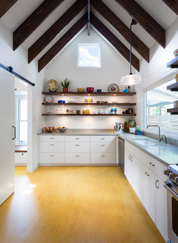 Bild på ett lantligt kök, med en undermonterad diskho, släta luckor, vita skåp, rostfria vitvaror och gult golv