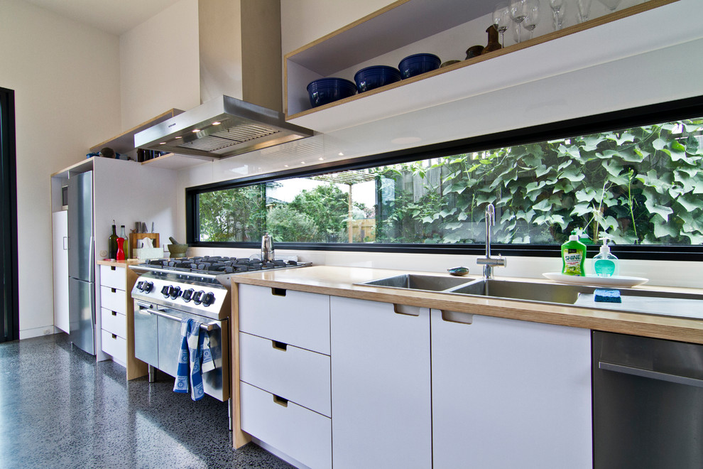 Example of a large urban galley concrete floor eat-in kitchen design in Melbourne with a double-bowl sink, flat-panel cabinets, white cabinets, wood countertops, white backsplash, glass sheet backsplash, stainless steel appliances and an island