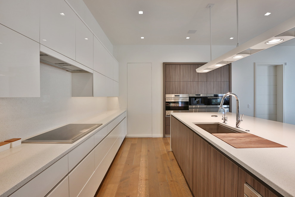Photo of a large modern u-shaped open plan kitchen in Columbus with a submerged sink, flat-panel cabinets, medium wood cabinets, composite countertops, white splashback, integrated appliances, medium hardwood flooring and an island.