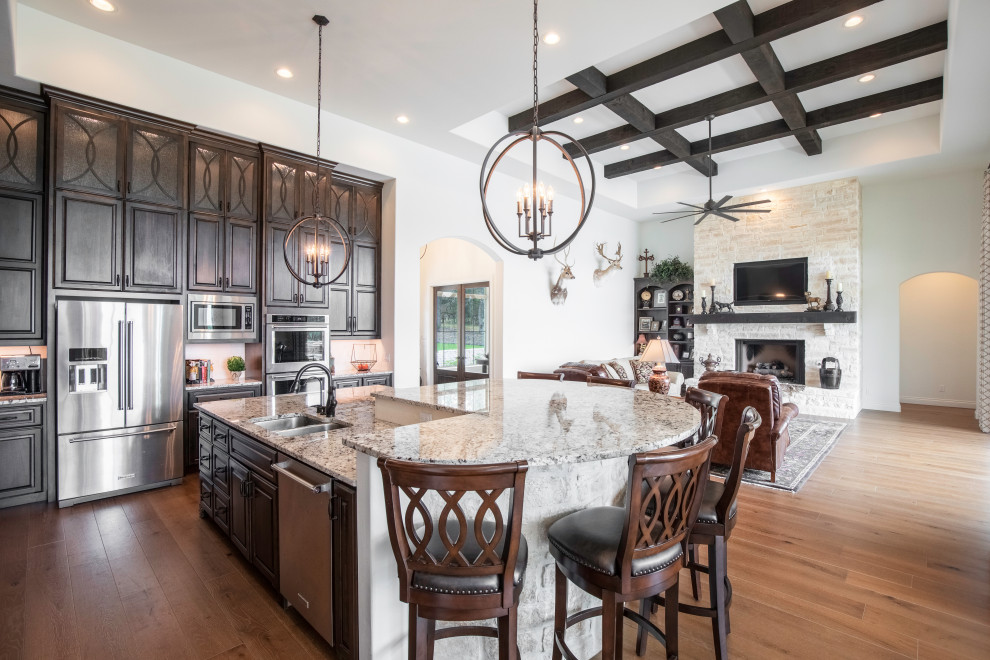 Example of a large tuscan galley medium tone wood floor and brown floor open concept kitchen design in Austin with an undermount sink, raised-panel cabinets, white backsplash, stainless steel appliances, no island, beige countertops and dark wood cabinets