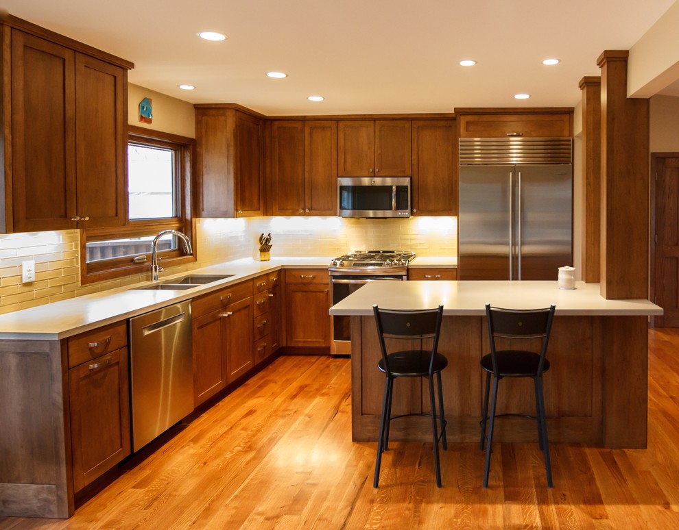 Minimalist l-shaped medium tone wood floor eat-in kitchen photo in Minneapolis with a double-bowl sink, shaker cabinets, medium tone wood cabinets, quartz countertops, glass tile backsplash, stainless steel appliances and an island