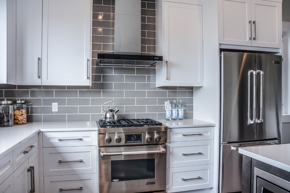 Enclosed kitchen - large modern l-shaped dark wood floor and brown floor enclosed kitchen idea in Calgary with an undermount sink, shaker cabinets, white cabinets, solid surface countertops, gray backsplash, subway tile backsplash, stainless steel appliances and a peninsula