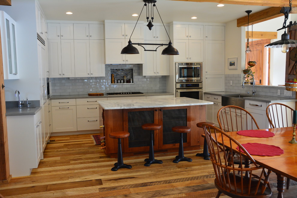 Rustik inredning av ett mellanstort grå grått kök, med en rustik diskho, skåp i shakerstil, vita skåp, bänkskiva i betong, grått stänkskydd, stänkskydd i glaskakel, integrerade vitvaror, mellanmörkt trägolv, en köksö och brunt golv