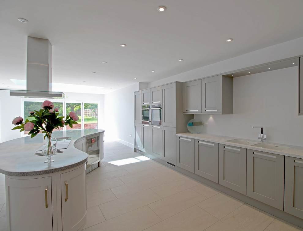 This is an example of a large contemporary l-shaped open plan kitchen in Essex with an integrated sink, shaker cabinets, grey cabinets, composite countertops, white splashback, black appliances, ceramic flooring and an island.