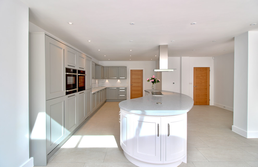 Photo of a large contemporary l-shaped open plan kitchen in Essex with an integrated sink, shaker cabinets, grey cabinets, composite countertops, white splashback, black appliances, ceramic flooring and an island.