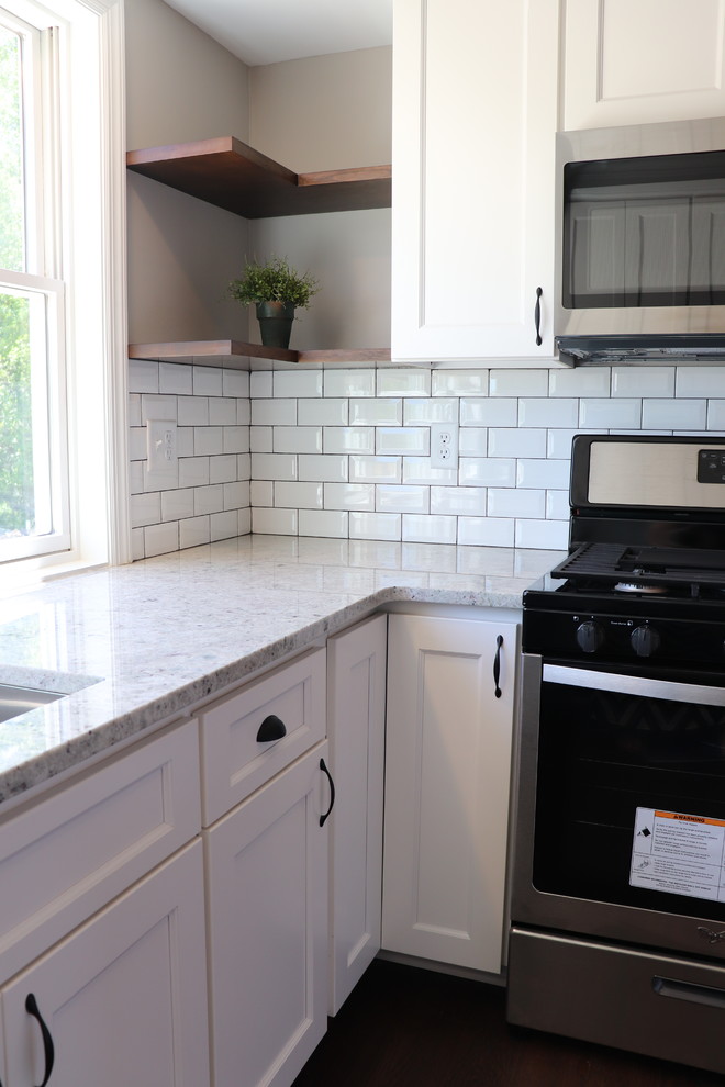 Foto på ett mycket stort lantligt grå kök, med en undermonterad diskho, skåp i shakerstil, vita skåp, granitbänkskiva, vitt stänkskydd, stänkskydd i tunnelbanekakel, rostfria vitvaror, mörkt trägolv, en halv köksö och brunt golv